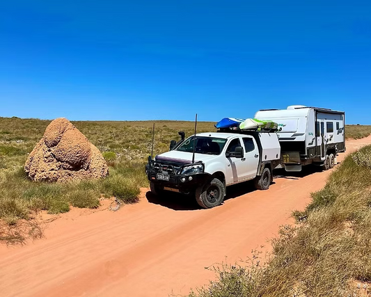 4WD ute towing a caravan on a red dirt outback track beside a termite mound — travelling Australia with Wild Touring